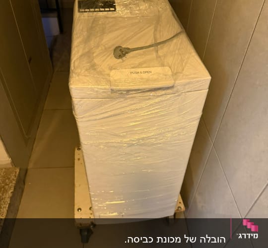 מכונת כביסה עטופה בניילון על גלגלים במסדרון